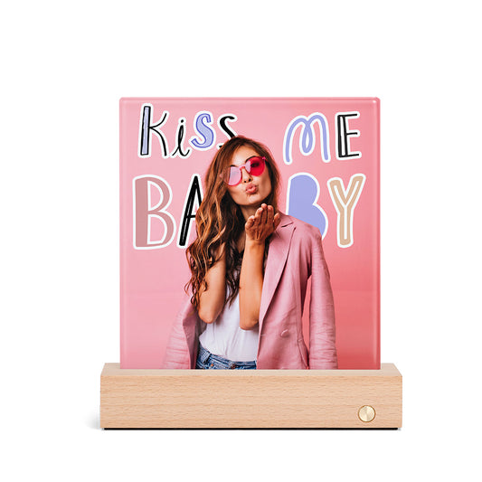 A stylish woman in sunglasses posing next to a pink glass art piece with the words 'Kiss Me Baby'.